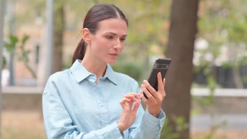 Woman Looks at Phone and Smiles Outdoors