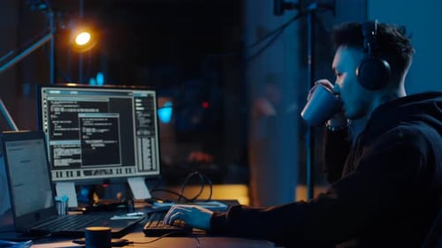 Un hacker asiatique codant une cyberattaque en buvant du café dans une pièce sombre la nuit
