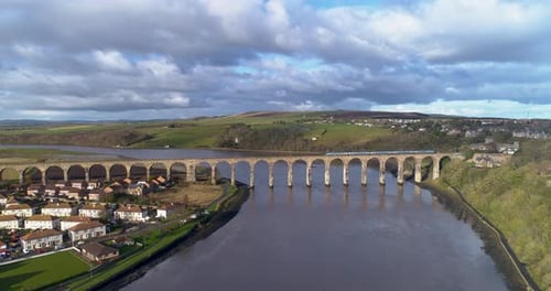 Aerial push-in shot over the River Tweed towards the rail bridge while train arrives into Berwick Up