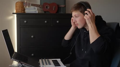 Focused Young Musician Composes in Home Studio with Laptop and Keyboard