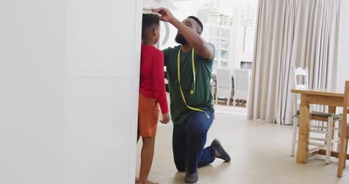 Happy african american father and son measuring height, in slow motion