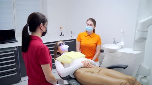 teeth whitening procedure in a dental clinic. female dentist or assistant uses modern equipment.