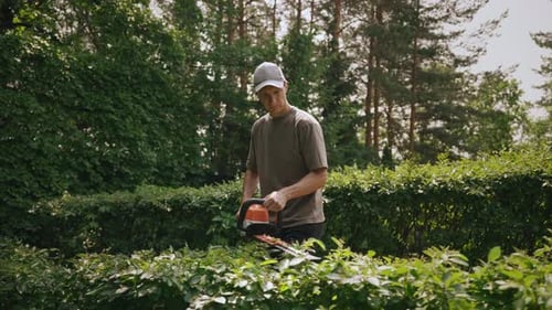 Professional Gardener Wearing Cap Trims Shrubs with Electric Hedge Trimmer Expert Landscape
