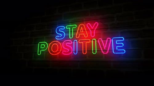 Símbolo de neón Stay Positive en una pared de ladrillo