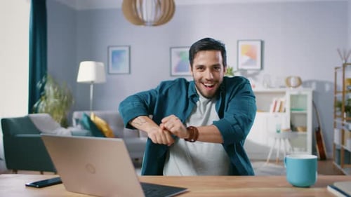 Un bel homme heureux fait une routine de danse amusante tout en étant assis à son bureau dans le salon.