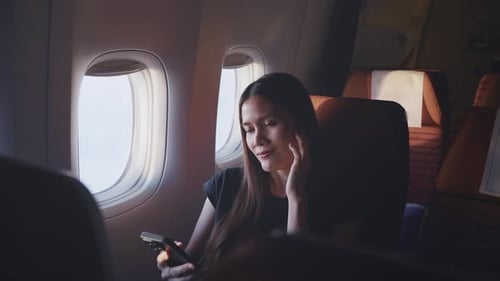 Asian woman using headphone listen to music while sitting in airplane.