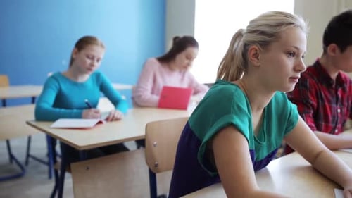 Teenage students studying in classroom at wooden desks
