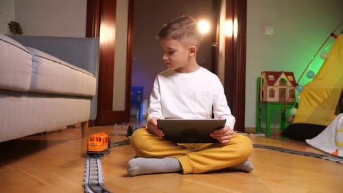 Boy Using Tablet with Toy Train Set