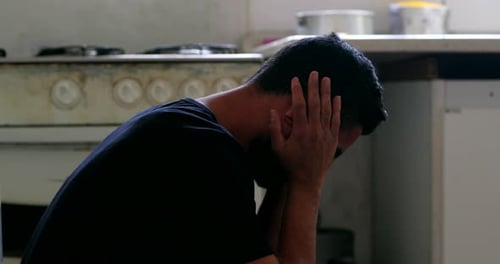 Man Covering Face with Hands in Kitchen Setting