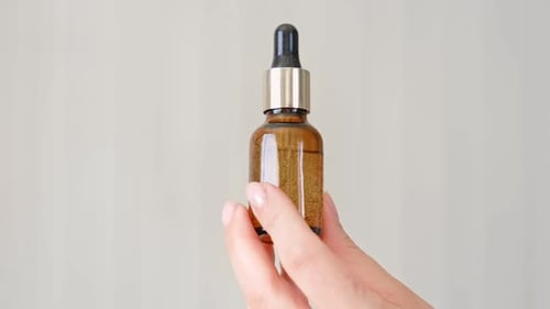Hand Holding Amber Glass Dropper Bottle with Cosmetic Oil