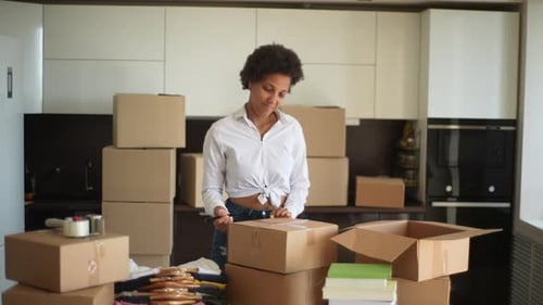 Portrait of Happy Smiling AfricanAmerican Young Woman Writing Label on Cardboard Box for Moving Out