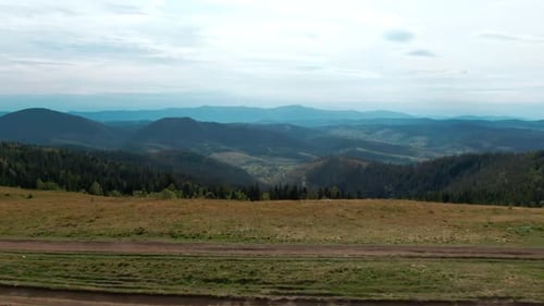Live Camera Moves Forward Along Hill Peak to Blue Carpathian Mountains at Background Aerial View