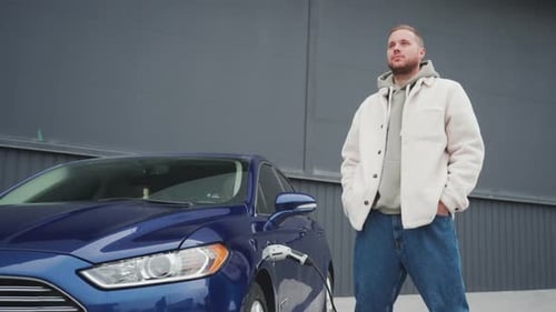 Man Stands by Charging Blue Electric Car