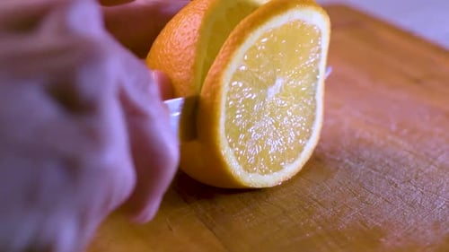 View of hand cutting an orange slice on a wooden board. Close up.