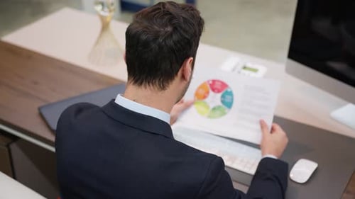 A CEO reviews a chart document at his office desk, analyzing data for business decisions