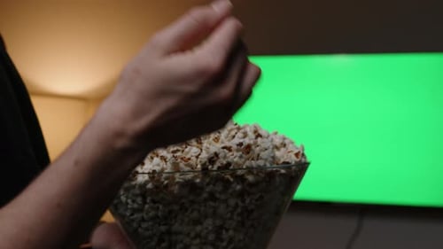 A woman eats popcorn in front of the television with a green screen. Mock-up with empty space.