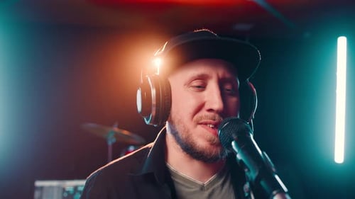 Portrait d'un homme barbu dans une casquette avec un casque dans un studio d'enregistrement chante dans un microphone et