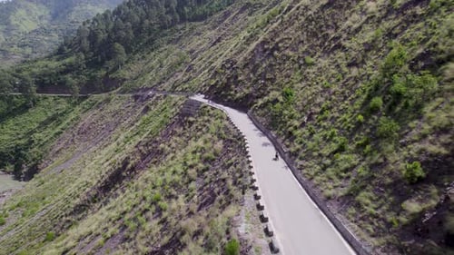 Aerial drone long shot of a man riding a bike with luggage traveling on an empty scenic road in a co