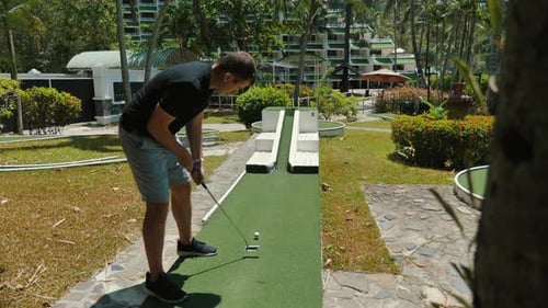 Man Playing Mini Golf at Tropical Resort with Lush Greenery Leisure