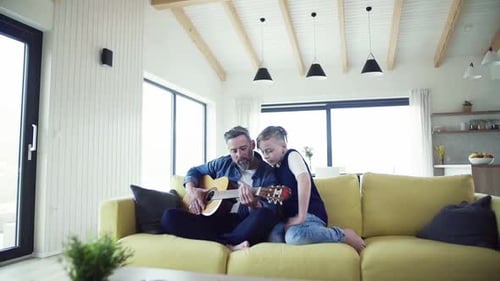 Man and boy playing guitar together on sofa