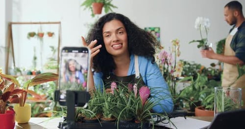 Mujer afroamericana florista en delantal grabando un vídeo en una floristería con el teléfono. Mujer hermosa