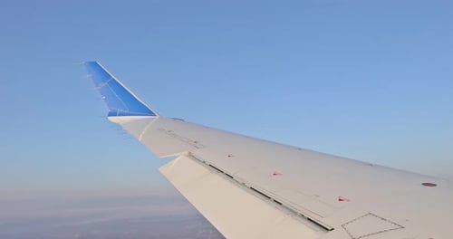 Wir sehen einen Flugzeugflügel, der sich über den Wolken erhebt und ein flauschiges Wolkenfenster hat