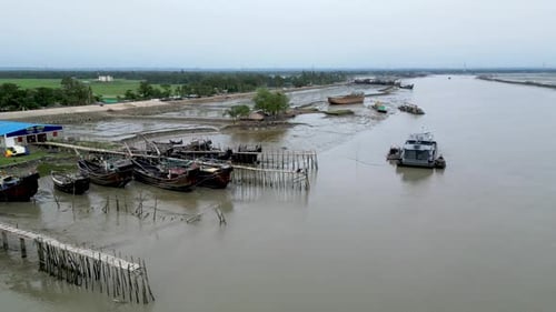 A jetty wharf lined with several fishing boats anchored along the river. The boats are moored to the