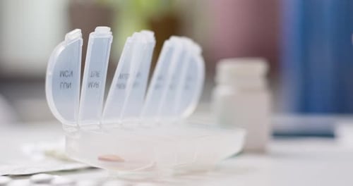 Male Hand Putting Pills Into Open Pill Organizer or Plastic Pillbox