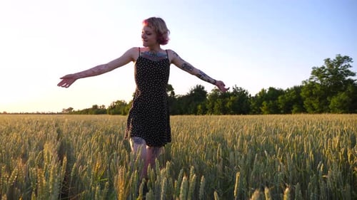 Young Hippie Woman in Dress Raising Hands While Goes Among Wheat Meadow and Enjoys Freedom Carefree
