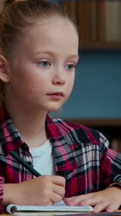 Focused Girl Writes in Notebook at Table Indoors