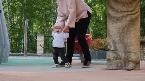 Baby Girl Learning to Walk with Mom on Playground
