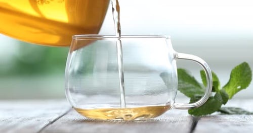 Pouring tea from teapot into glass cup at table against blurred background, closeup