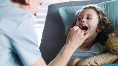 Female doctor gently examining a small girl patient in hospital bed