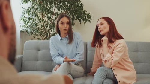 Two Women Talk on Couch Indoors