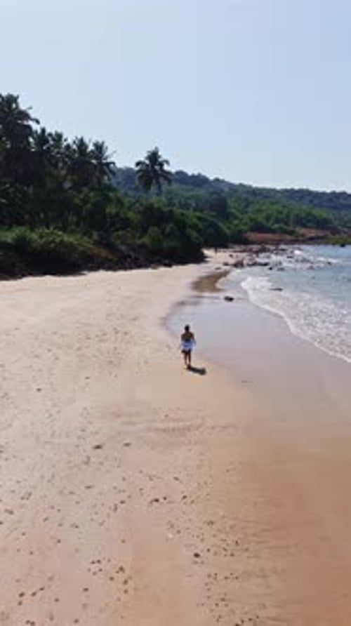 Portrait drone shot following a girl on a promenade at a beach, sunny day