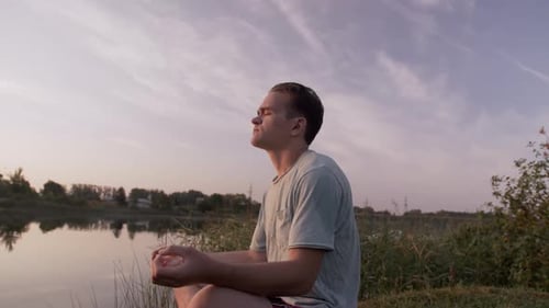 Young Adult Meditating Beside Quiet Lake at Sunset