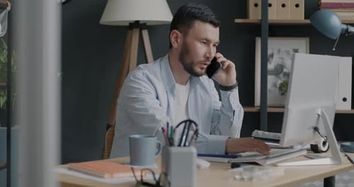 Portrait of Young Biracial Man Working with Computer and Talking on Mobile Phone in Office