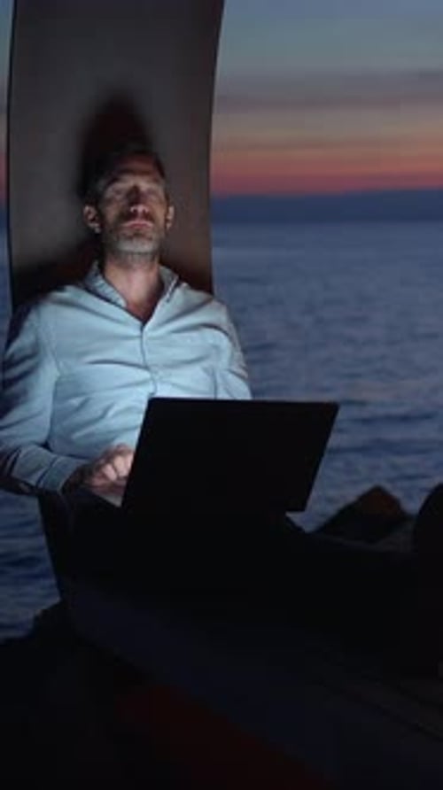 A Man Works Remotely By the Sea at Sunset Blending Work and Relaxation Perfectly