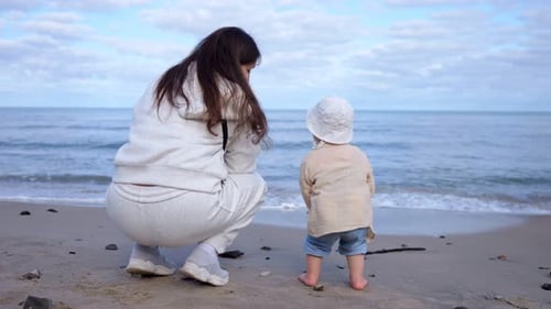 Mum with Child Looks at Clear Sea Squatting on Sandy Beach