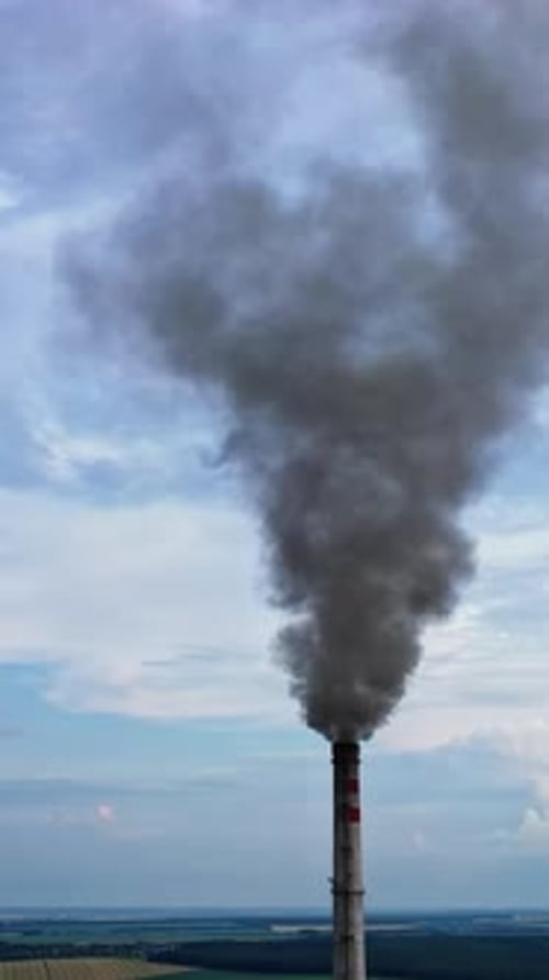 View from the drone at the old aged weathered tall industrial factory chimney with smoke over it.