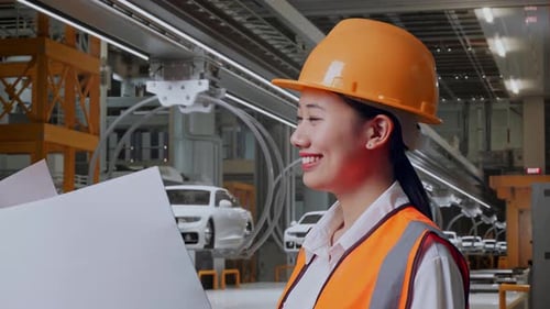 Une ingénieure asiatique regarde un plan entre ses mains dans une usine de voitures électriques