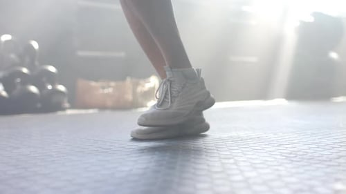 Jumping in white sneakers, man exercising in gym with sunlight streaming in