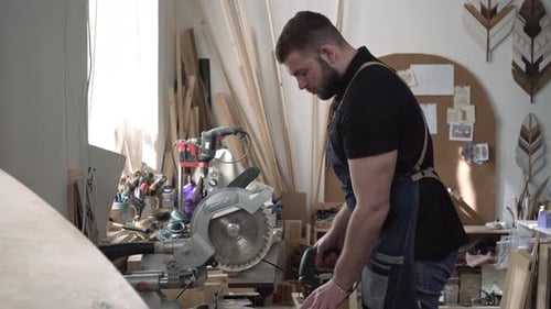 The Carpenter Works in the Workshop Sawing Wood and Making Furniture