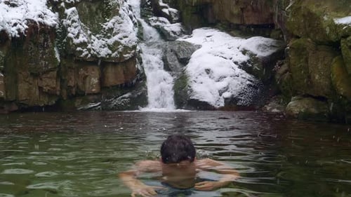 Man plunges in cold water during ice swimming in subzero cold river by the beautiful waterfall in sn