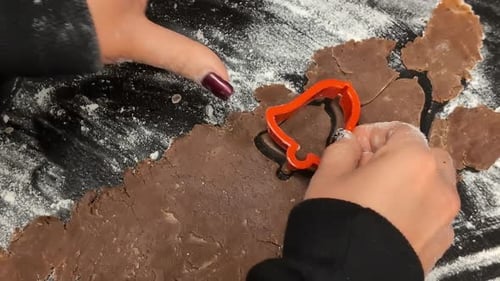 Using a cookie cutter to cut bell-shaped gingerbread Christmas cookies