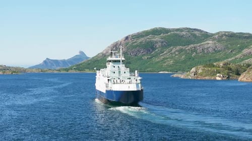 Drone track ferry sailing in fjord toward pointed arctic Norway mountain