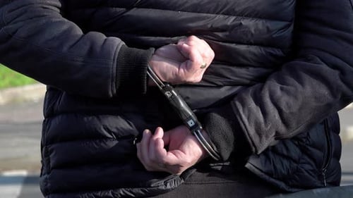 A person stands detained with his hands restrained with speed cuffs behind his back.