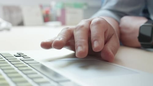 Close-up of a man's hand scrolling and tapping on a laptop trackpad in a modern office