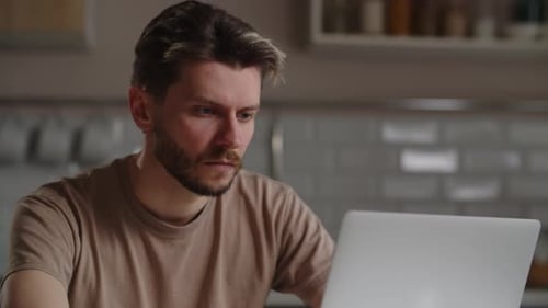 Seriöser Mann tippt auf der Laptop-Tastatur in der Küche Ein Freelancer arbeitet remote an einem Computer