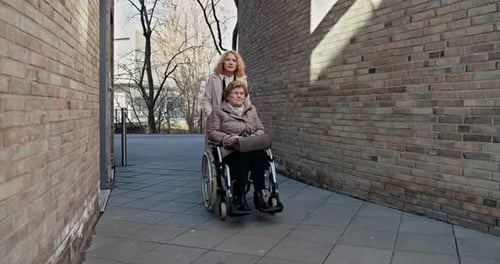Woman Pushing Senior Woman in Wheelchair Outdoors